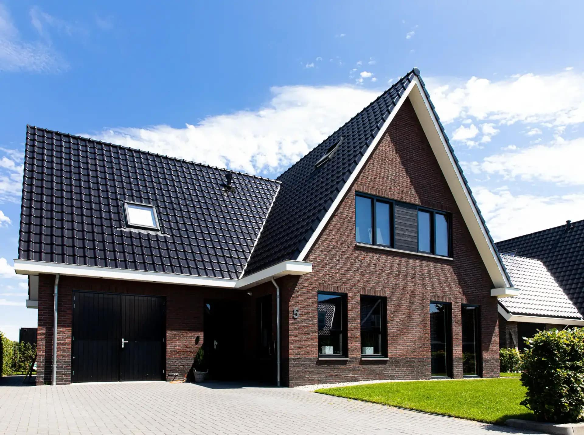 Traditionele T-kapwoning in Wolvega met bakstenen gevel, zwart dak, grote raampartijen en carport, gezien vanaf de voortuin