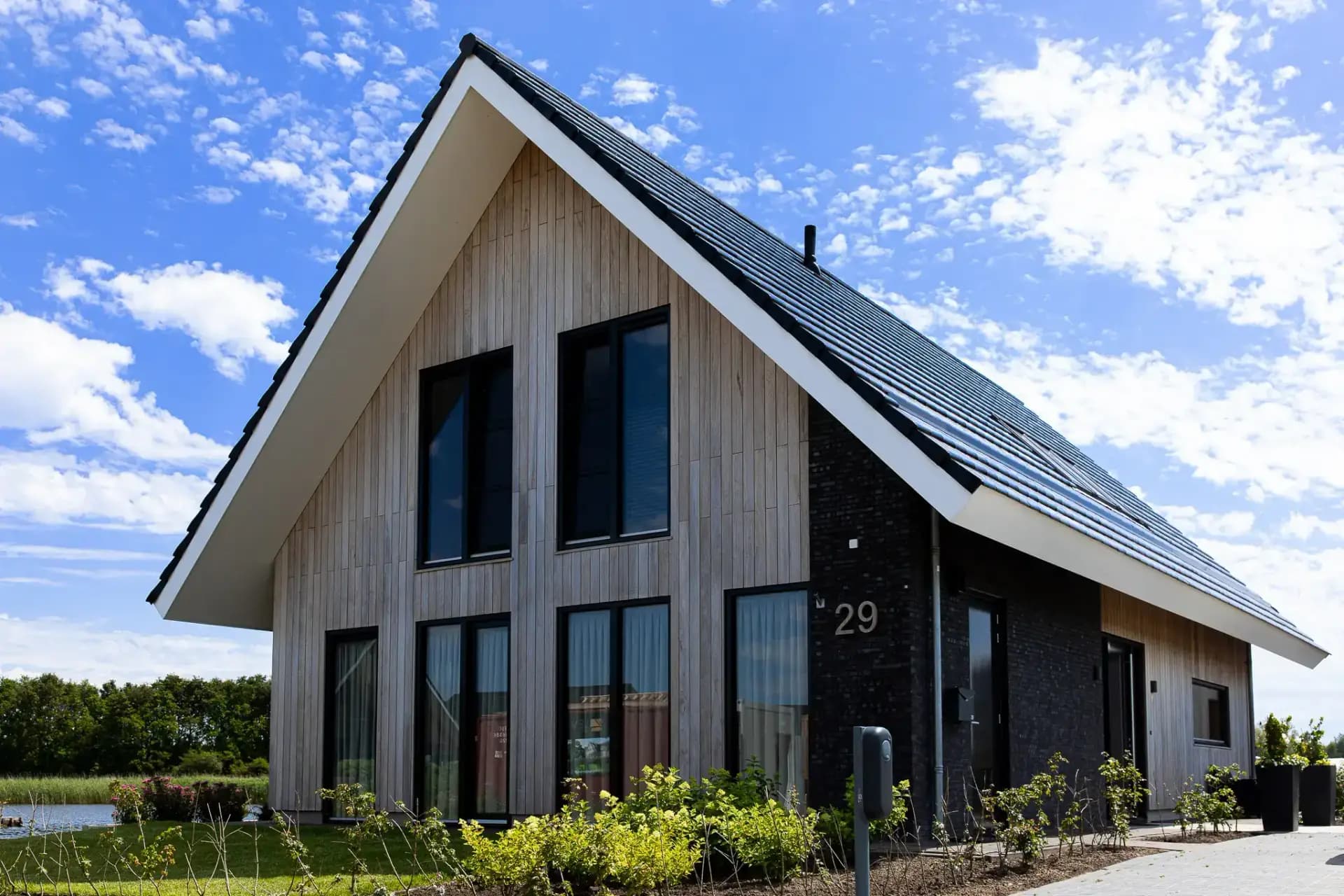 Schuurwoning op een kopkavel aan het Icarusblauwtje in Wolvega, in naturel hout met langformaat metselwerkaccenten en panoramisch uitzicht op het water.