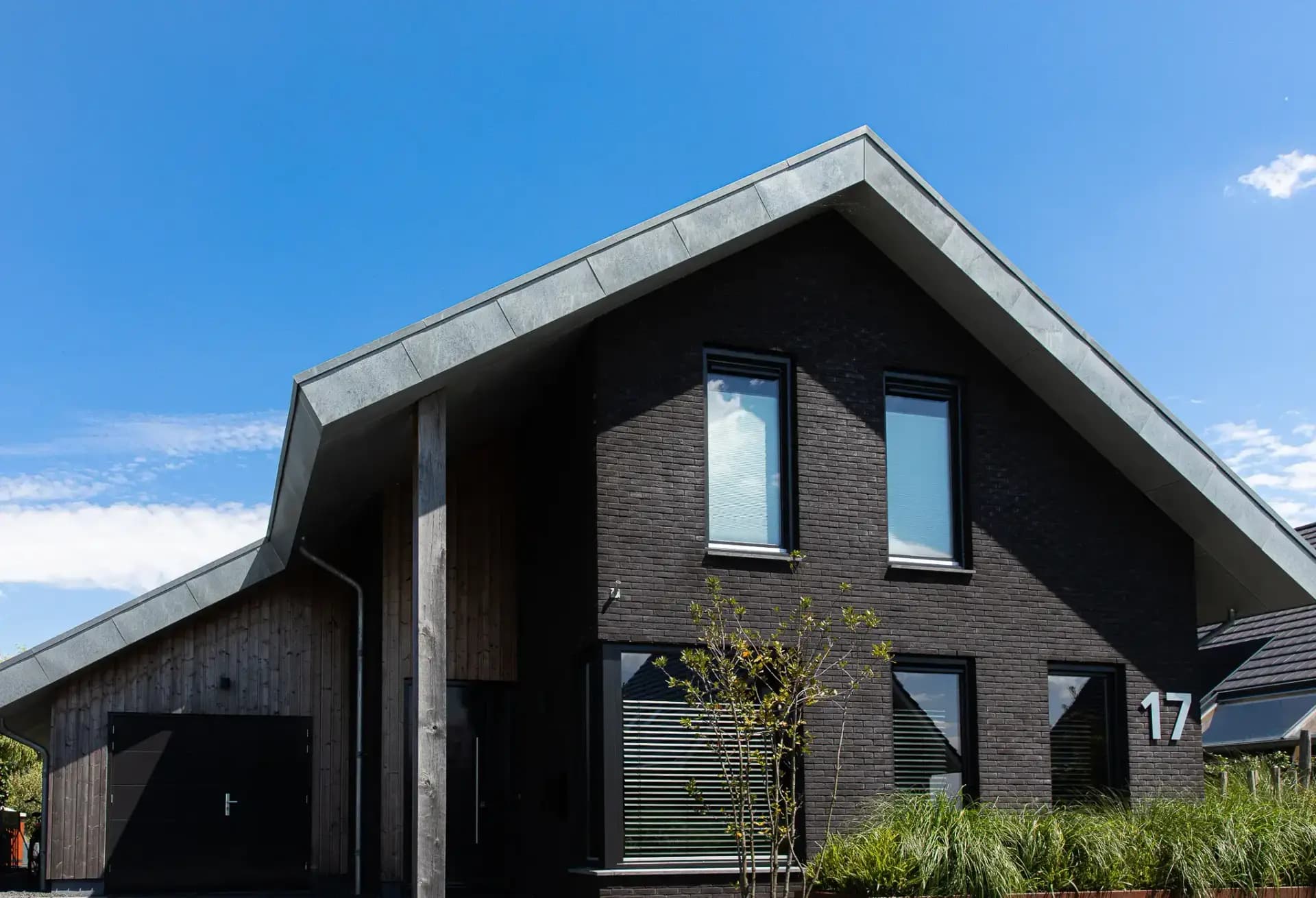 Minimalistische eigentijdse woning in Wolvega met overhangend asymmetrisch dak, hoekkozijnen, donker metselwerk, vergrijzend hout en zinken dakrand.