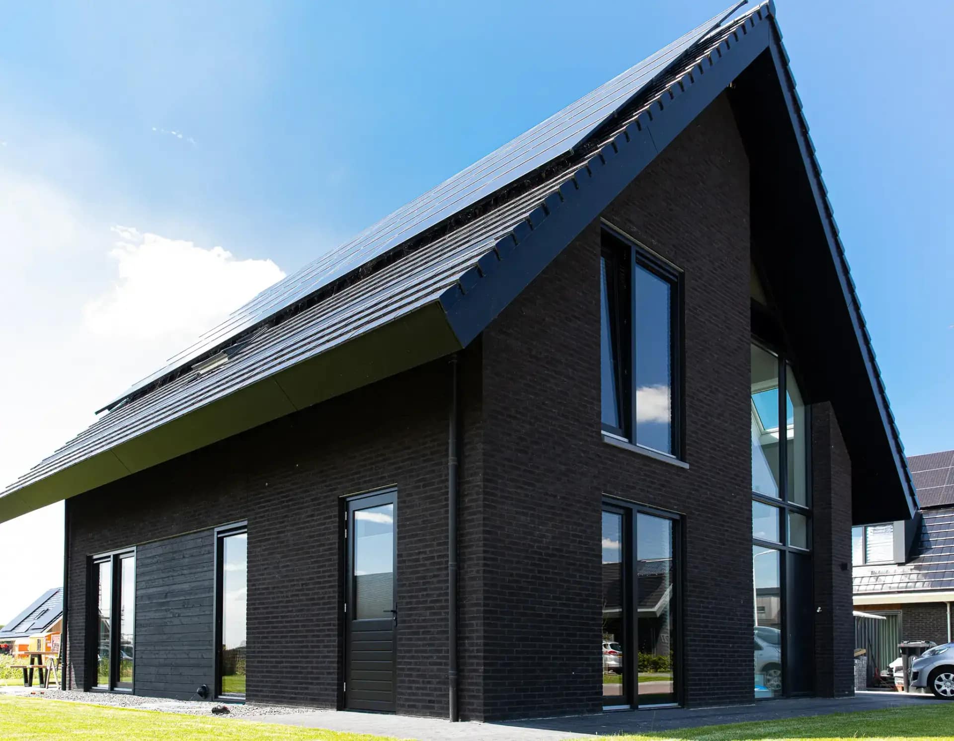 Moderne woning Wolvega met zwarte bakstenen gevel, grote raampartijen en schuin dak met groene accenten, gezien vanaf tuinzijde