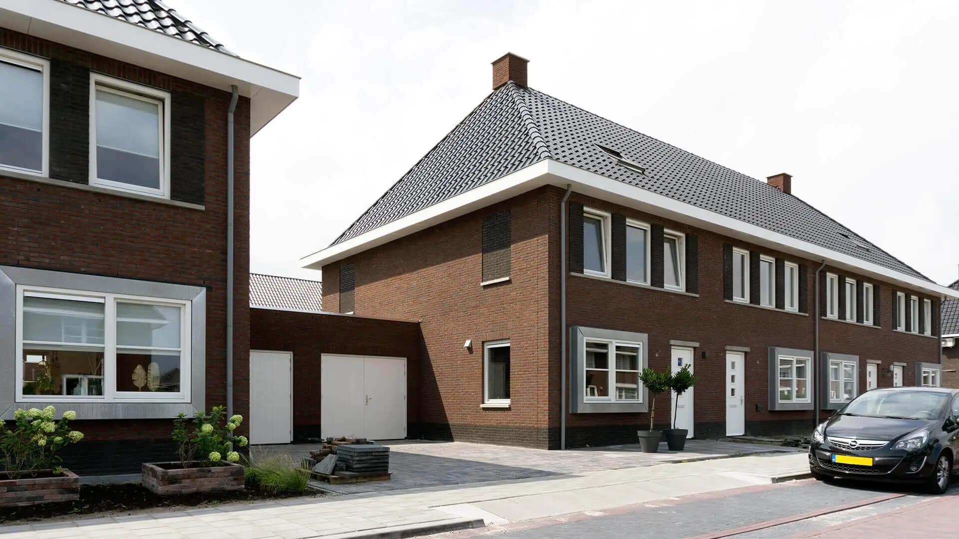 Nieuwbouwproject 14 rijwoningen Wolvega: moderne bakstenen gevels met witte kozijnen, grijze daken, witte garagedeuren en aangelegde voortuin
