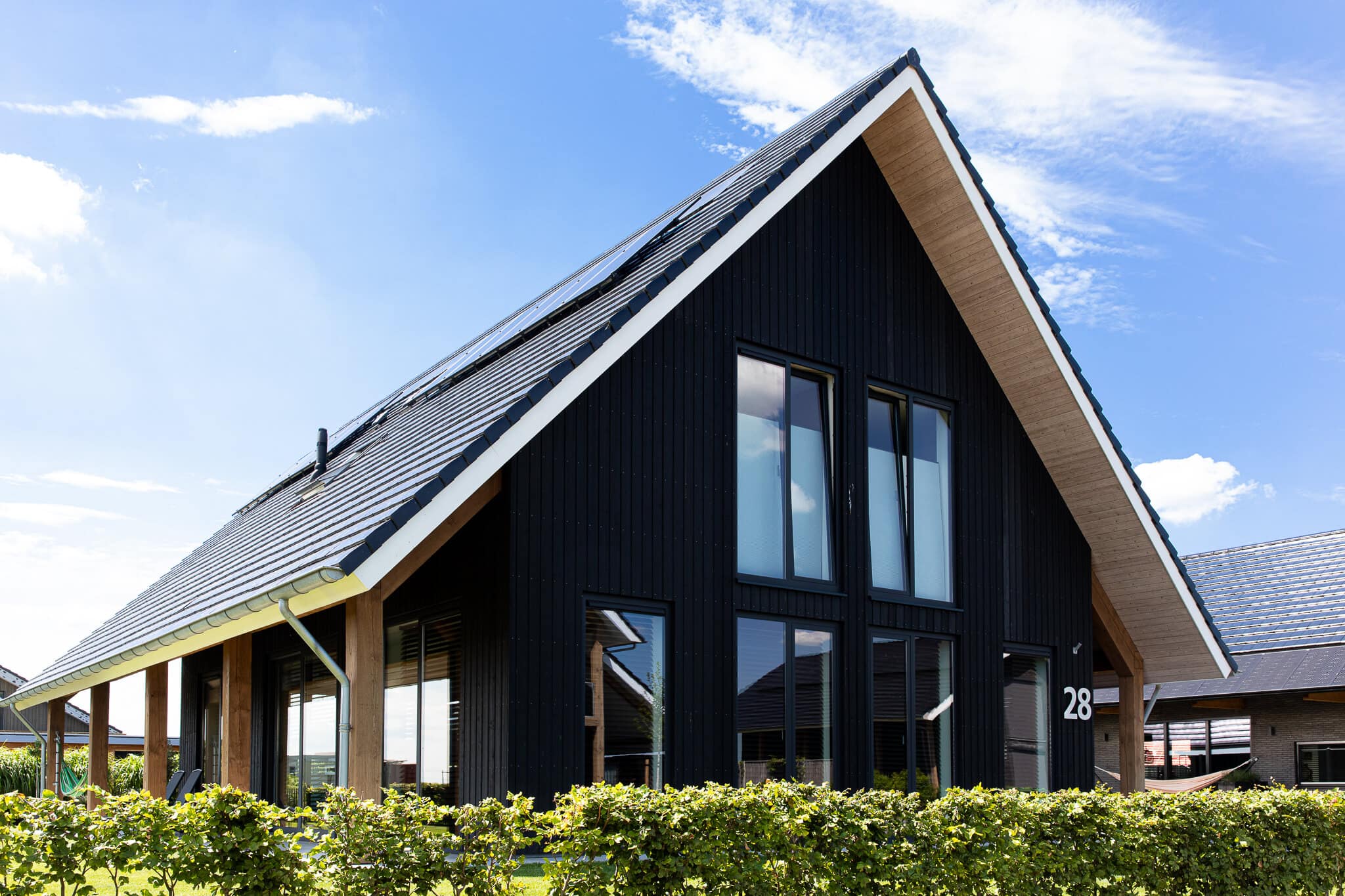 Moderne zwarte schuurwoning in Wolvega met houten accenten, grote raampartijen en hellend dak, omgeven door groene haag