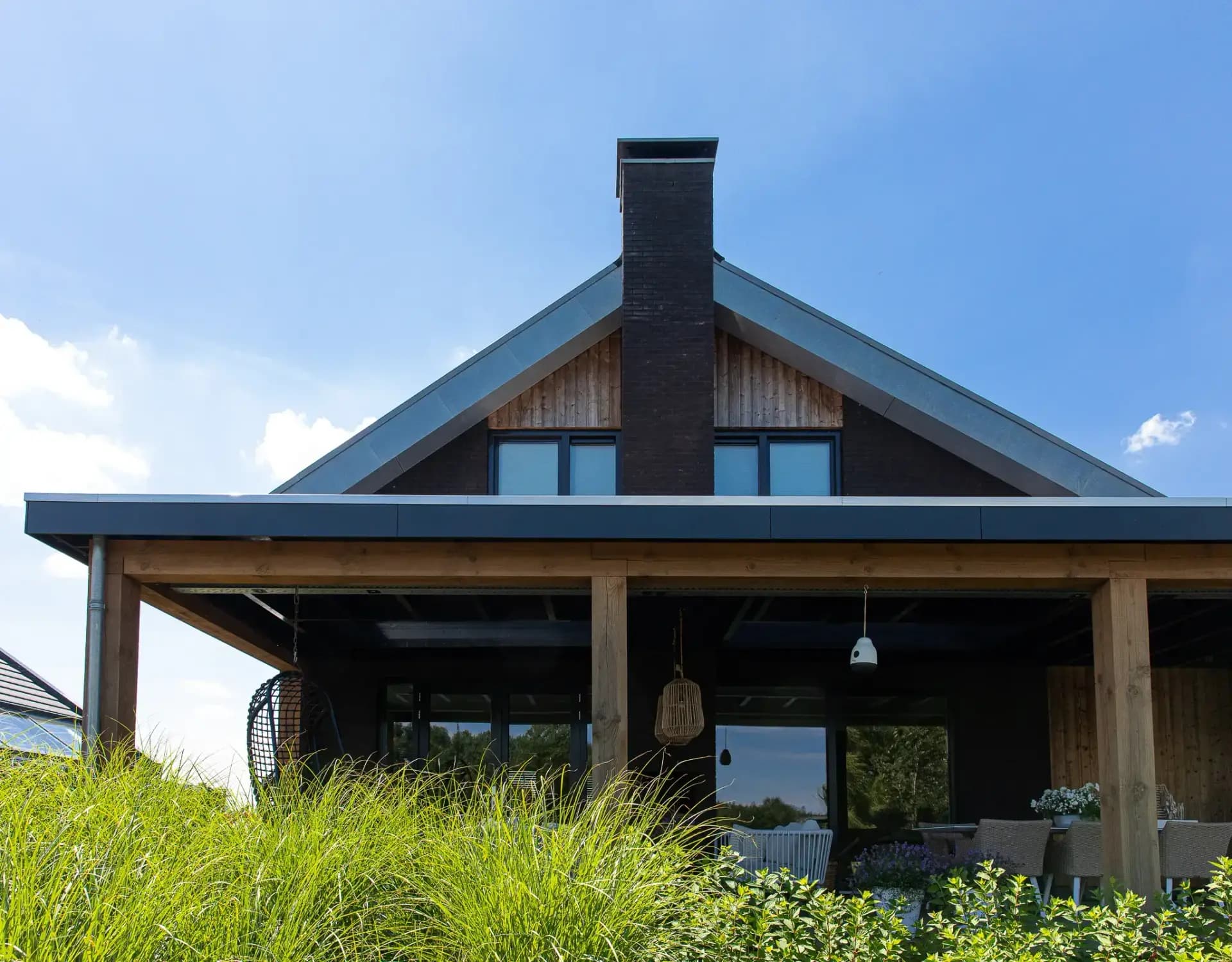 Minimalistische eigentijdse woning in Wolvega met overhangend asymmetrisch dak, hoekkozijnen, donker metselwerk, vergrijzend hout en zinken dakrand.