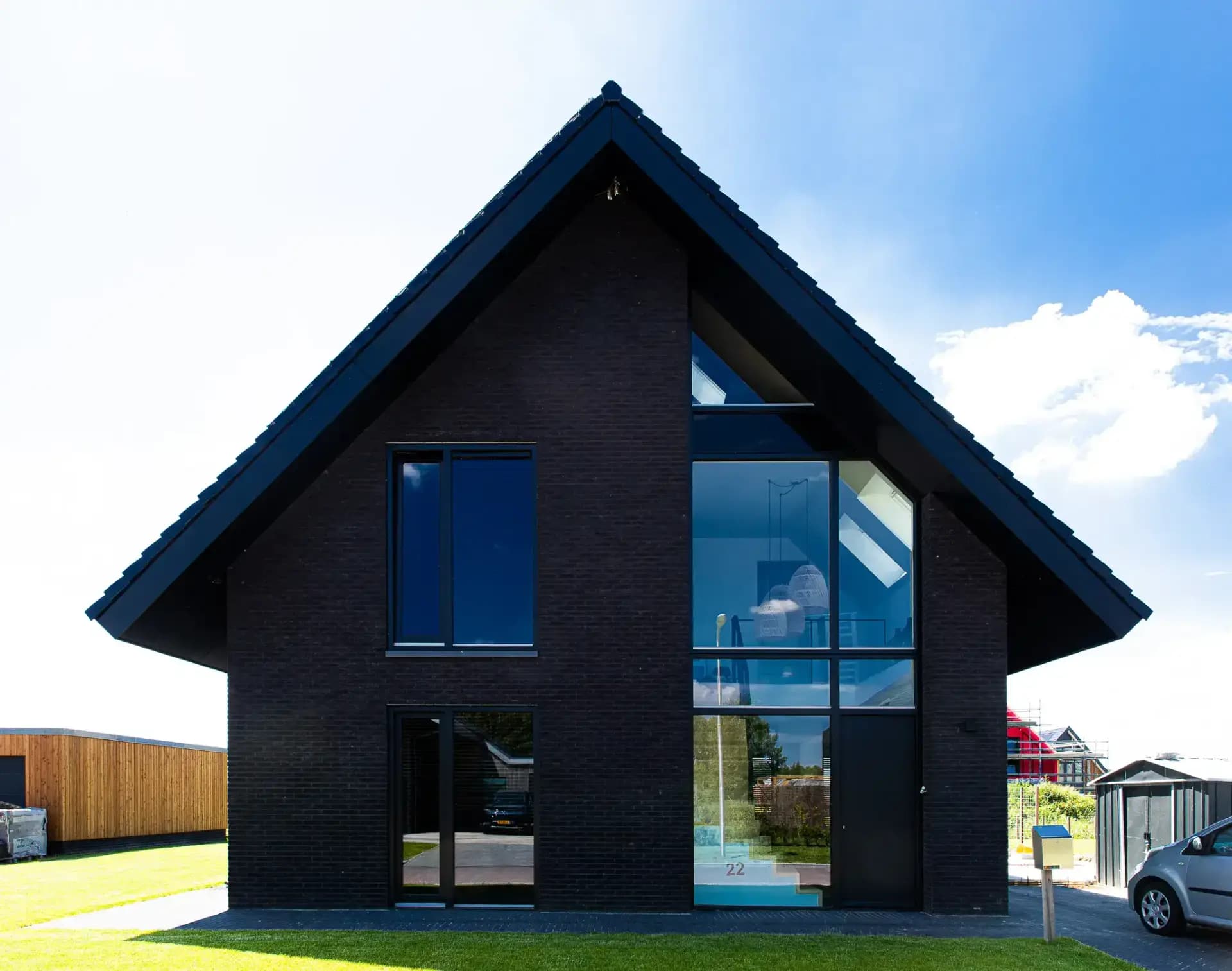 Minimalistisch woonhuis in Wolvega met donkere esthetiek, grote glasoppervlakken, lamellen en houten gevelbekleding in een beperkt kleurenpalet.
